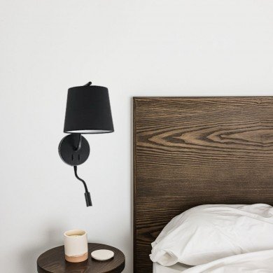 Applique murale moderne avec abat-jour noir près d'un lit et d'une table de chevet ronde.