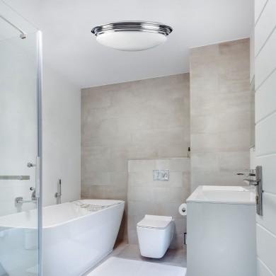Luminaire dans une salle de bain moderne avec plafonnier blanc et miroir, sur fond de douche, baignoire et toilettes. Quel luminaire mettre dans une salle de bain.