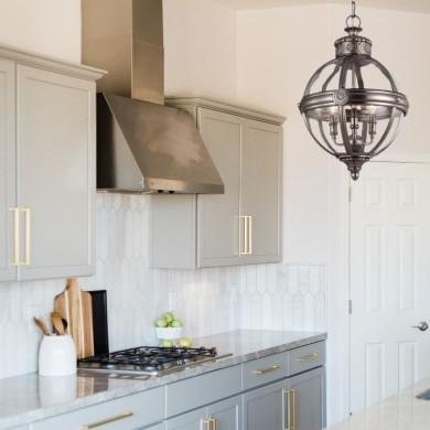 Lustre design noir suspendu au-dessus d'une cuisine moderne, éclairage métal, près d'armoires gris clair et plan de travail. | comment choisir son lustre de salle à manger