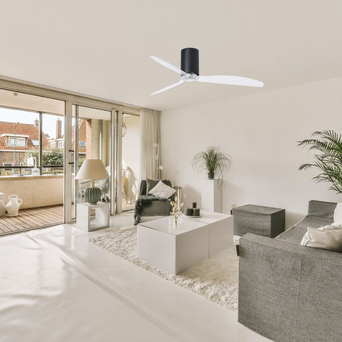 Meilleur ventilateur efficace pour supporter la canicule : plafond blanc moderne dans un salon clair, ventile au-dessus, canapé gris et table basse, ouverture sur balcon.
