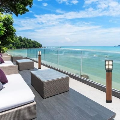 Terrasse en bord de mer avec canapé et ottomane en rotin, éclairage extérieur moderne et lampe solaire pour piscine le long de la rambarde.