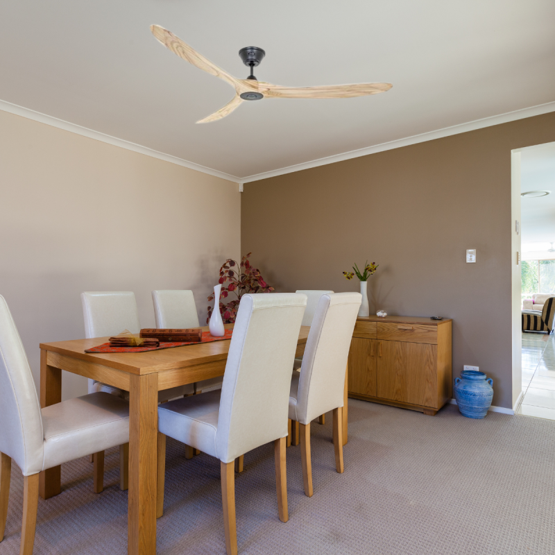 Ventilateur de plafond design en bois au-dessus d’une salle à manger, table en bois et chaises capitonnées, décoration naturelle et ambiance chaleureuse.